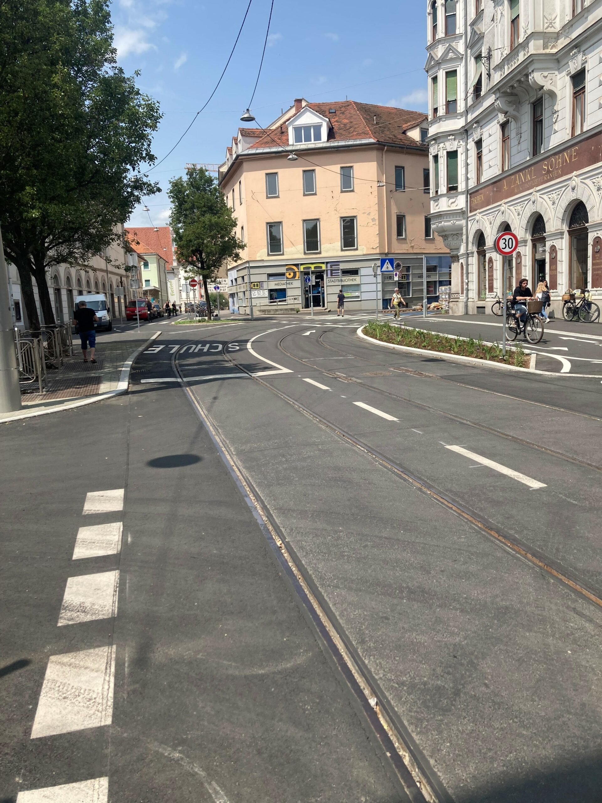 Straßenansicht in Graz mit Straßenbahnschienen und Gebäuden.