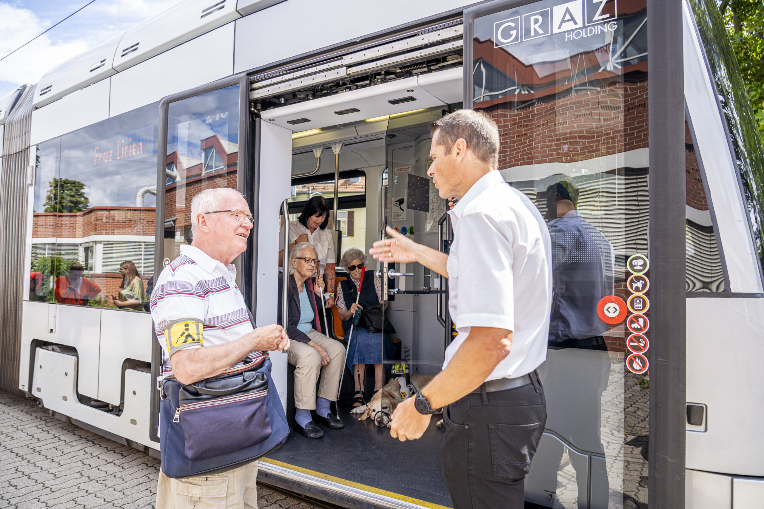 Ein Mann hilft Senioren beim Einsteigen in eine Graz Holding Straßenbahn.