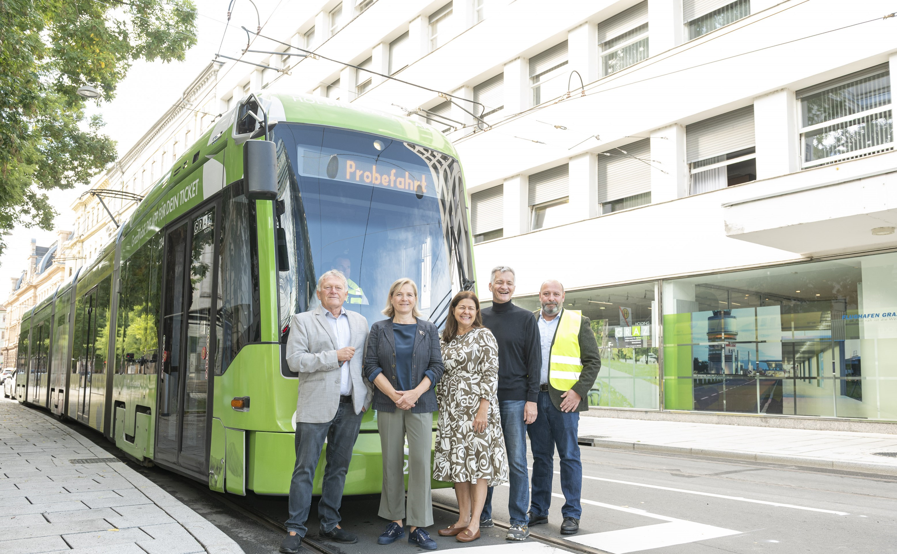Fünf Personen vor einer grünen Straßenbahn in Graz, "Probefahrt".