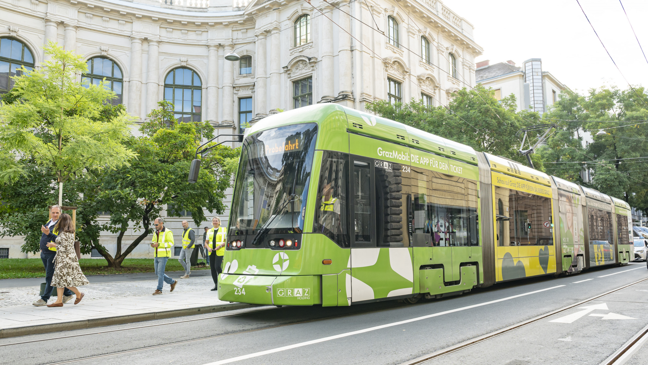 Grüne Graz-Straßenbahn "GrazMobil: Die App für Dein Ticket" fährt.