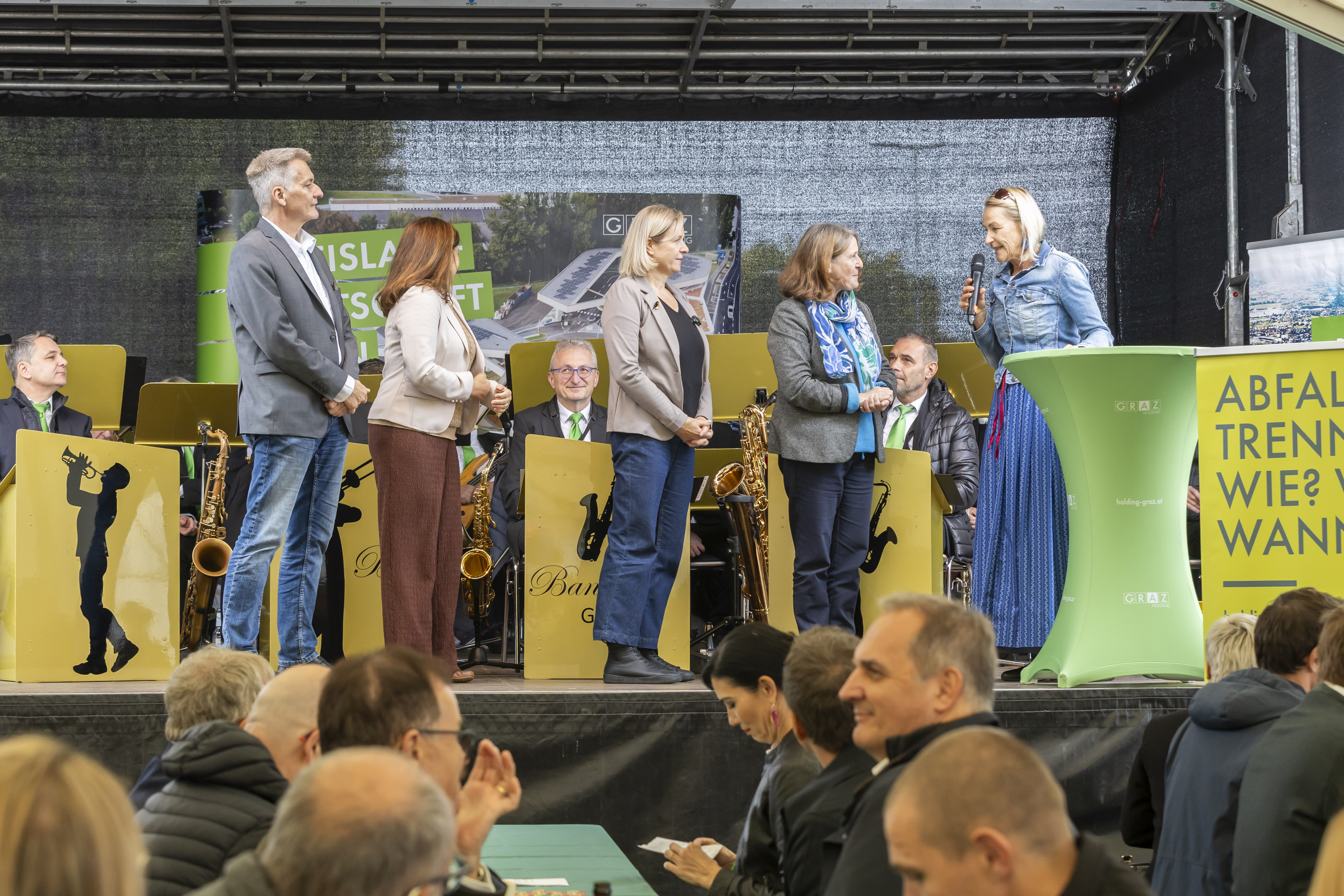 Personen auf Bühne in Graz mit Band und Abfall-Trennungs-Schild.