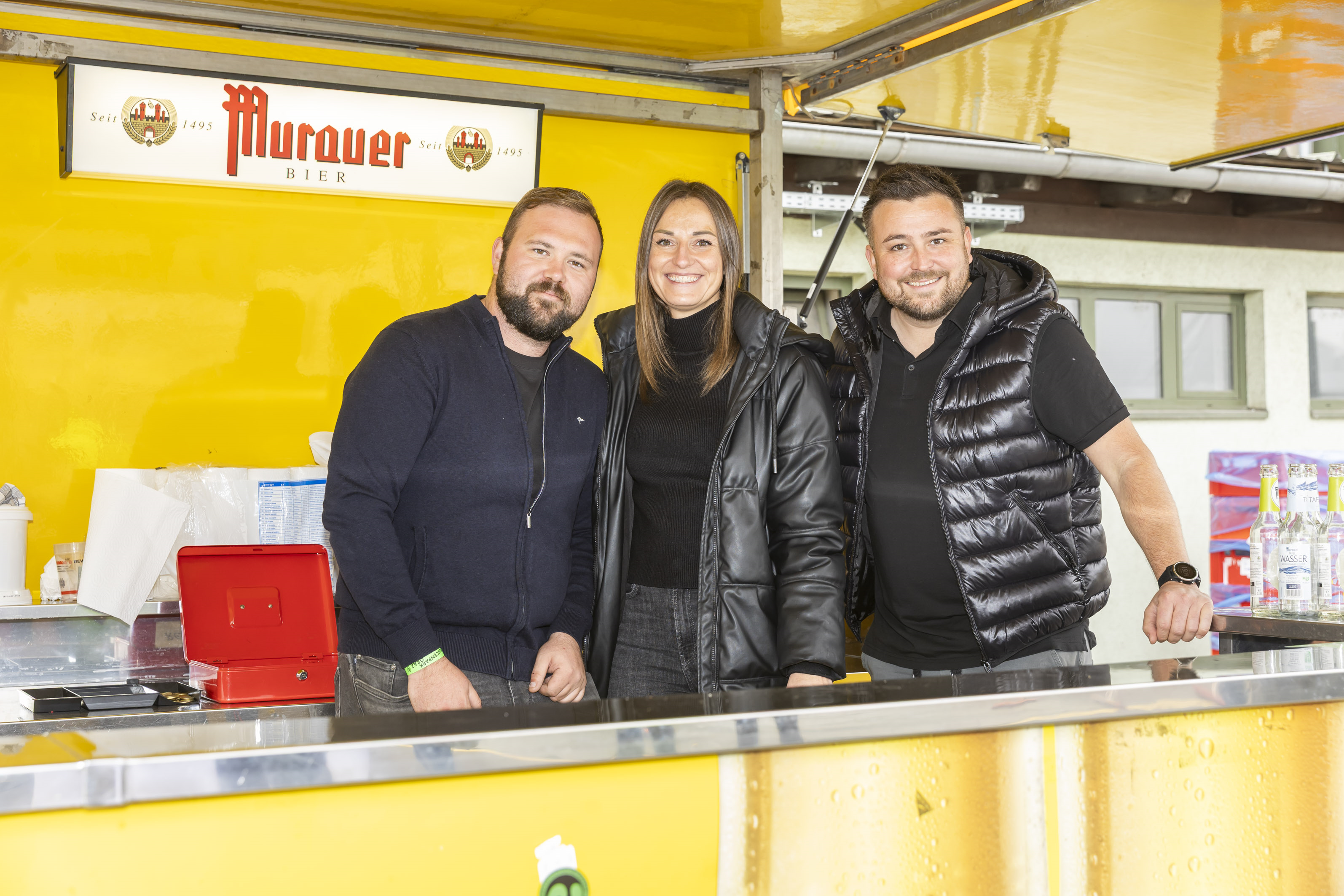 Drei Personen stehen hinter einem Murauer Bierstand in Graz.