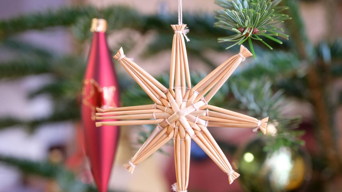 Weihnachtsbaum mit Strohstern und rotem Ornament.
