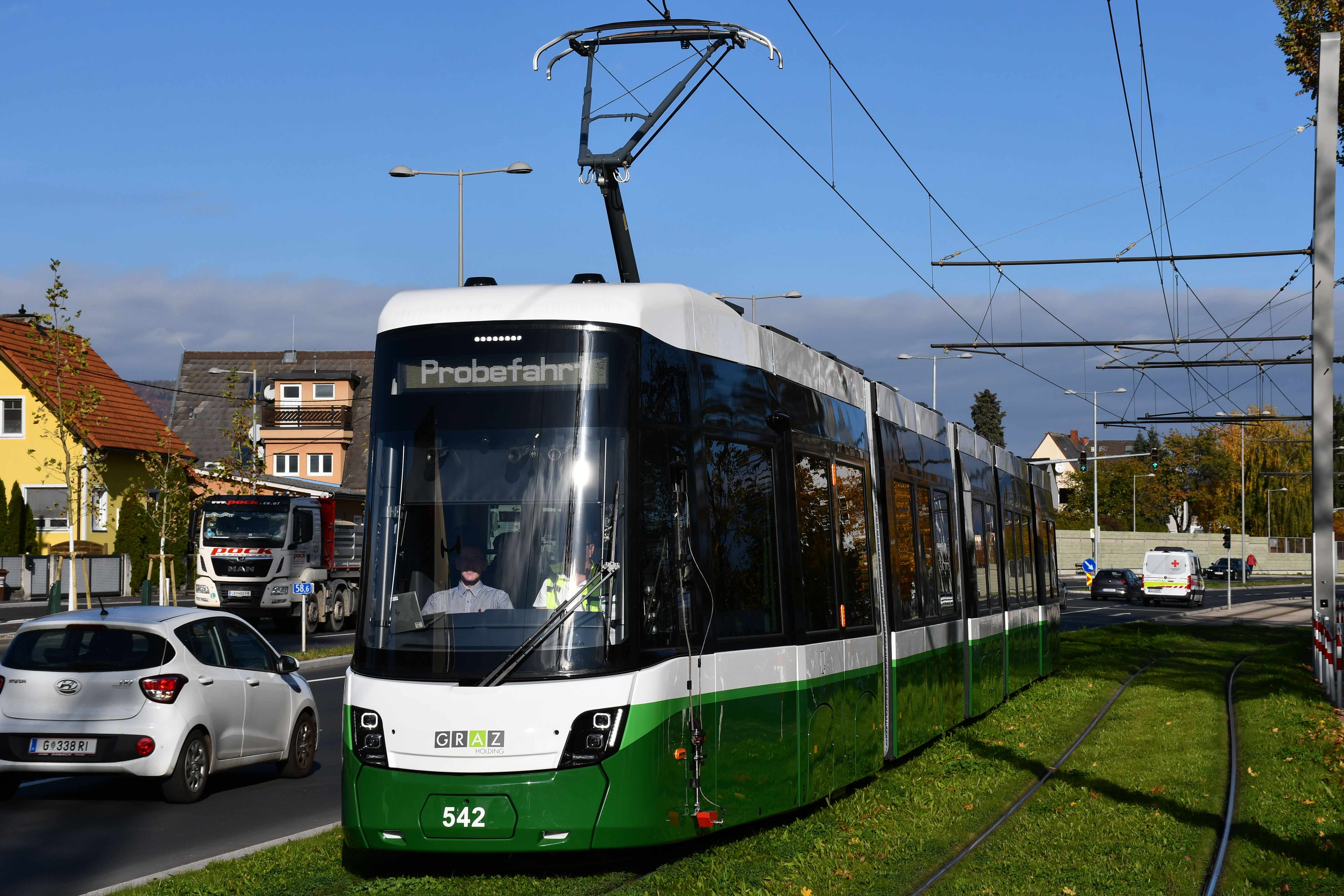Grüne Straßenbahn Graz "Probefahrt" mit Nummer 542 fährt auf Gleisen.