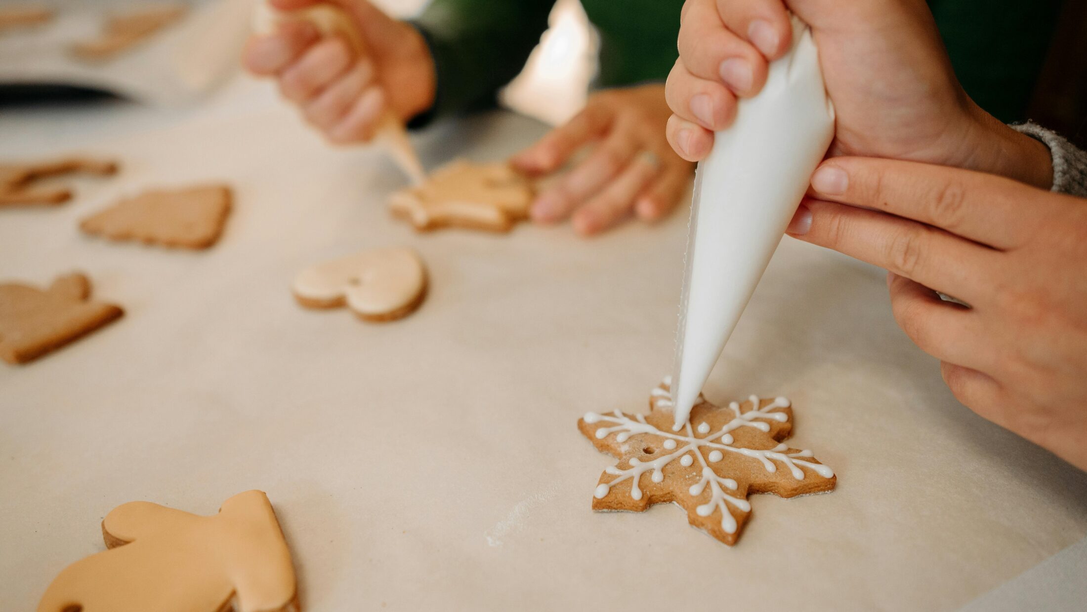Zwei Personen verzieren Lebkuchen mit weißem Zuckerguss.