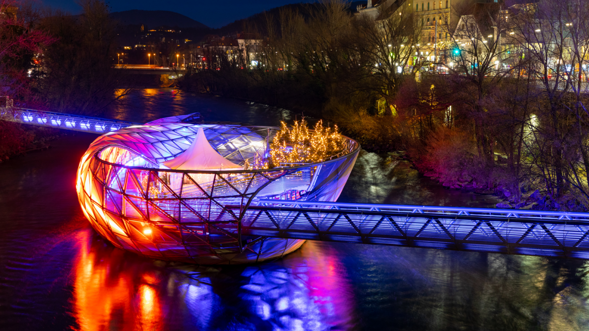 Nachts: Murinsel, Graz, beleuchtet mit Steg über den Fluss.