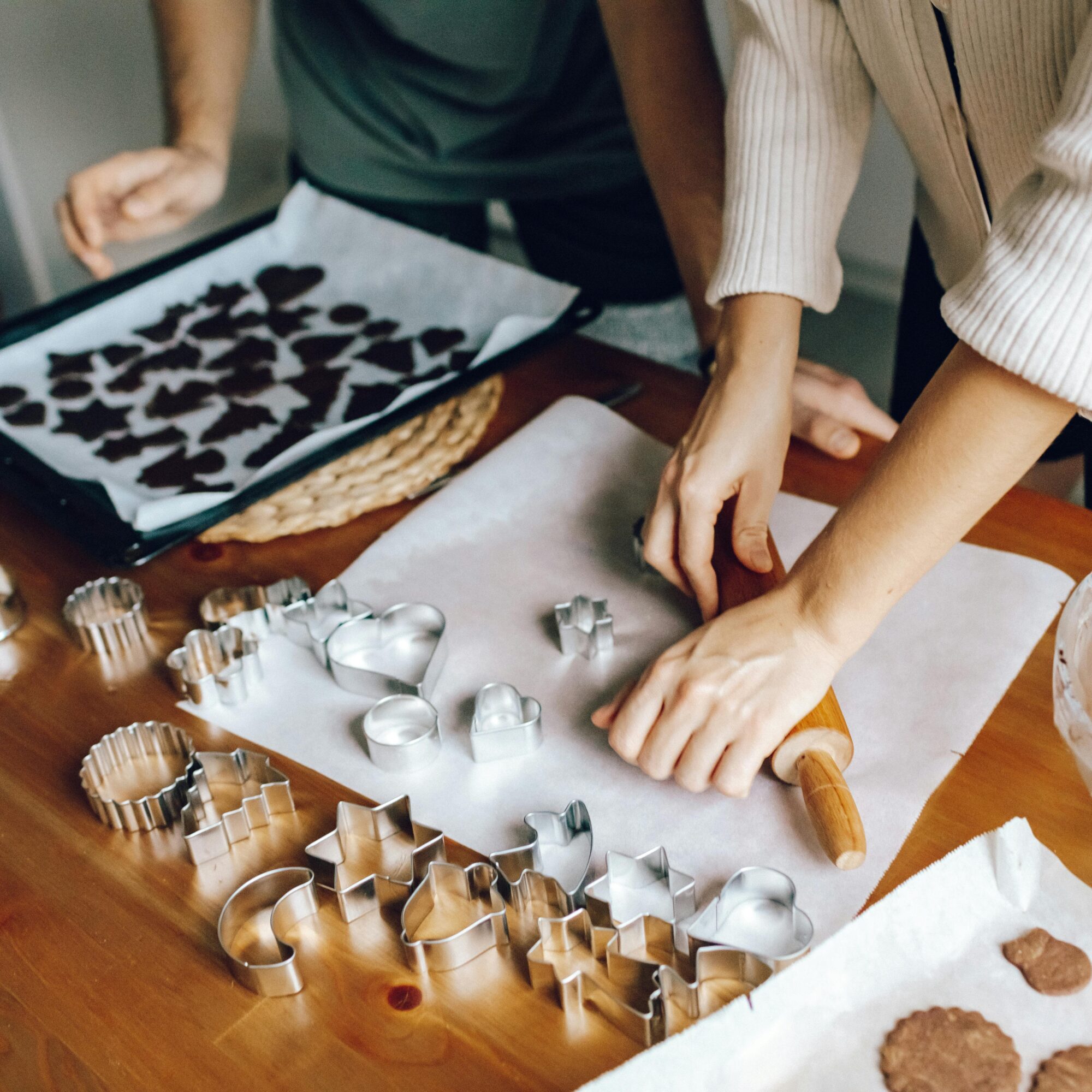 Zwei Personen backen Kekse. Teig wird ausgerollt, Förmchen und Backblech mit Keksen sind zu sehen.