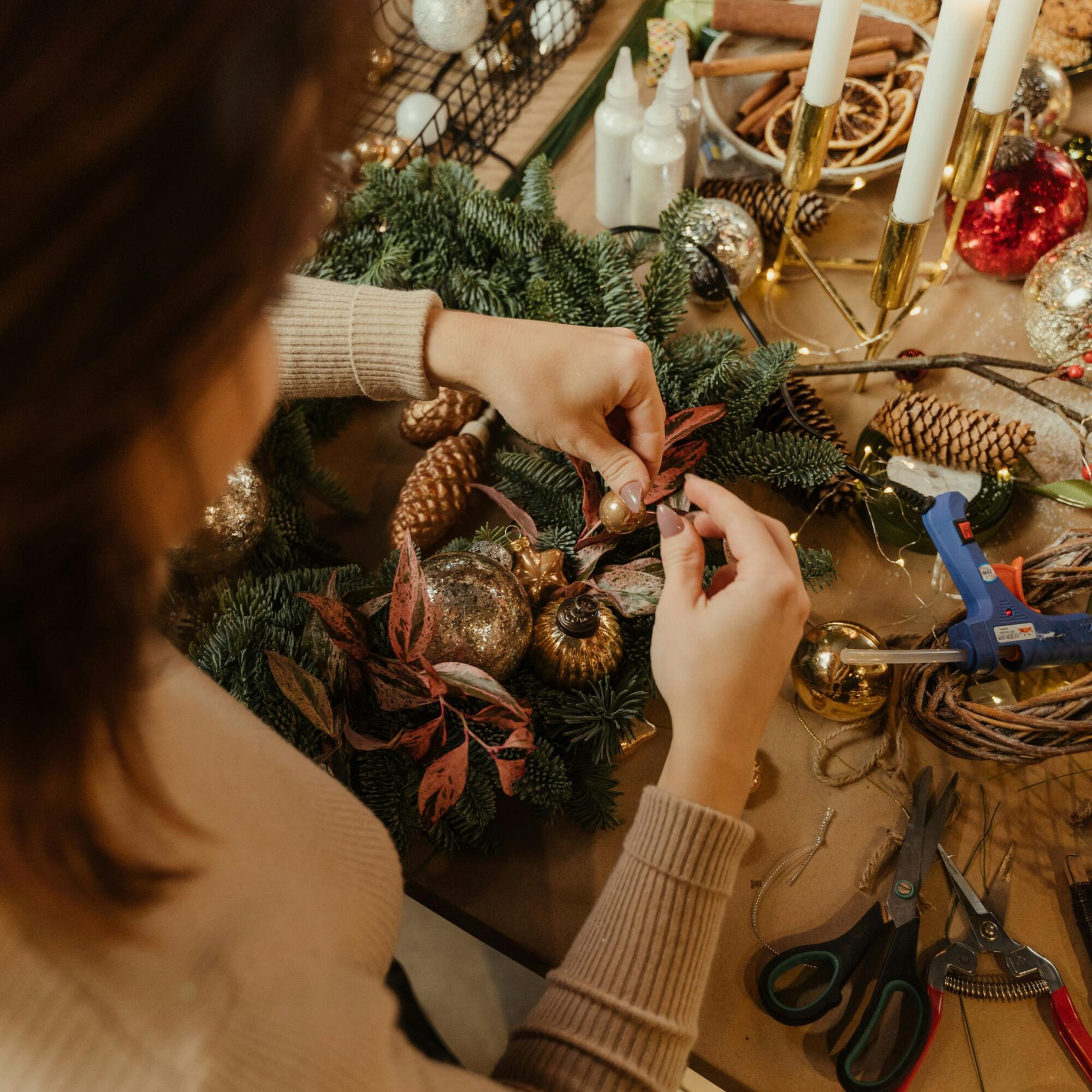 Frau fertigt Weihnachtskranz mit Schmuck und Werkzeug an.