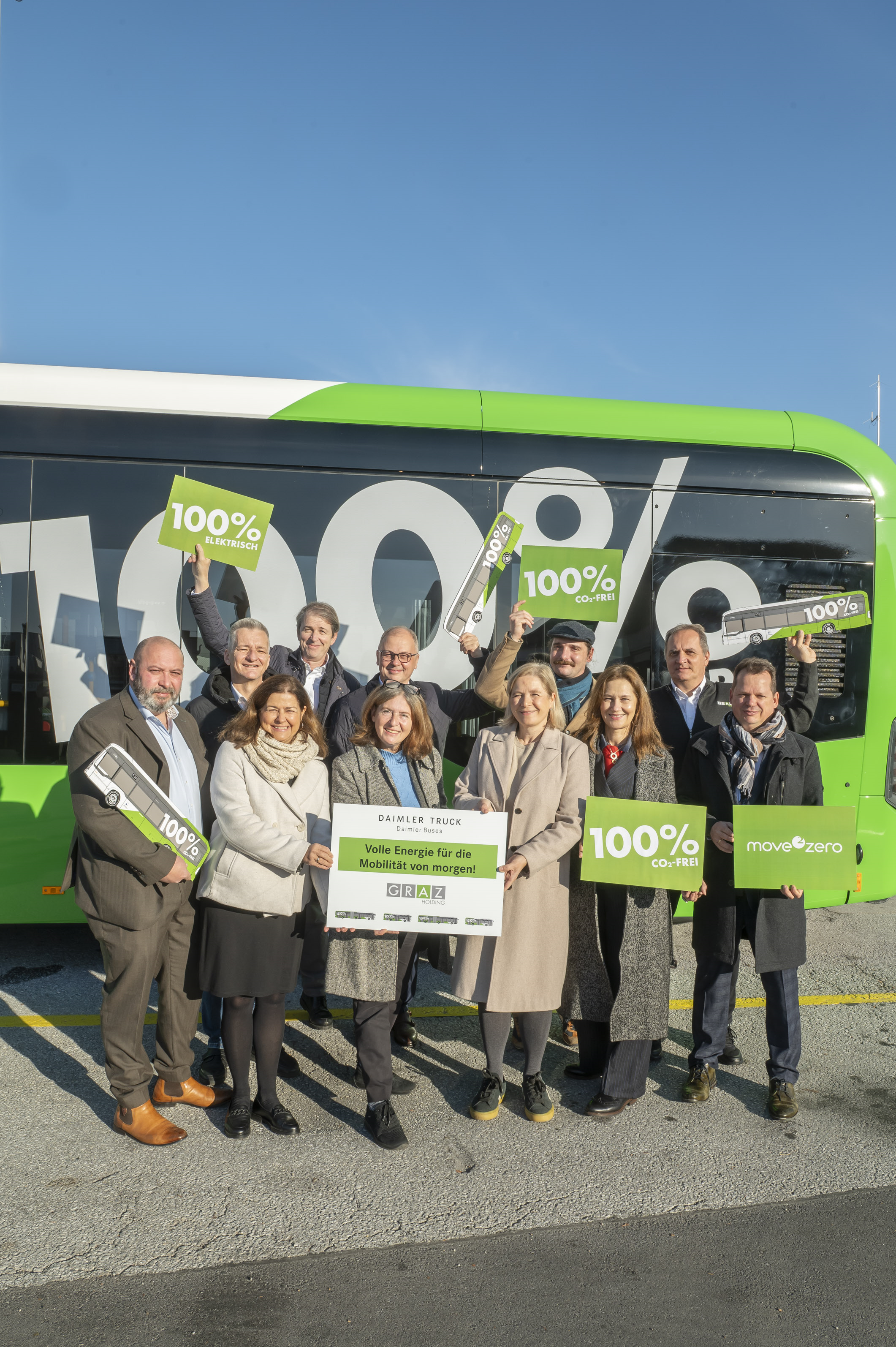 Eine Gruppe von Leuten steht vor einem Bus in Graz und hält Schilder.