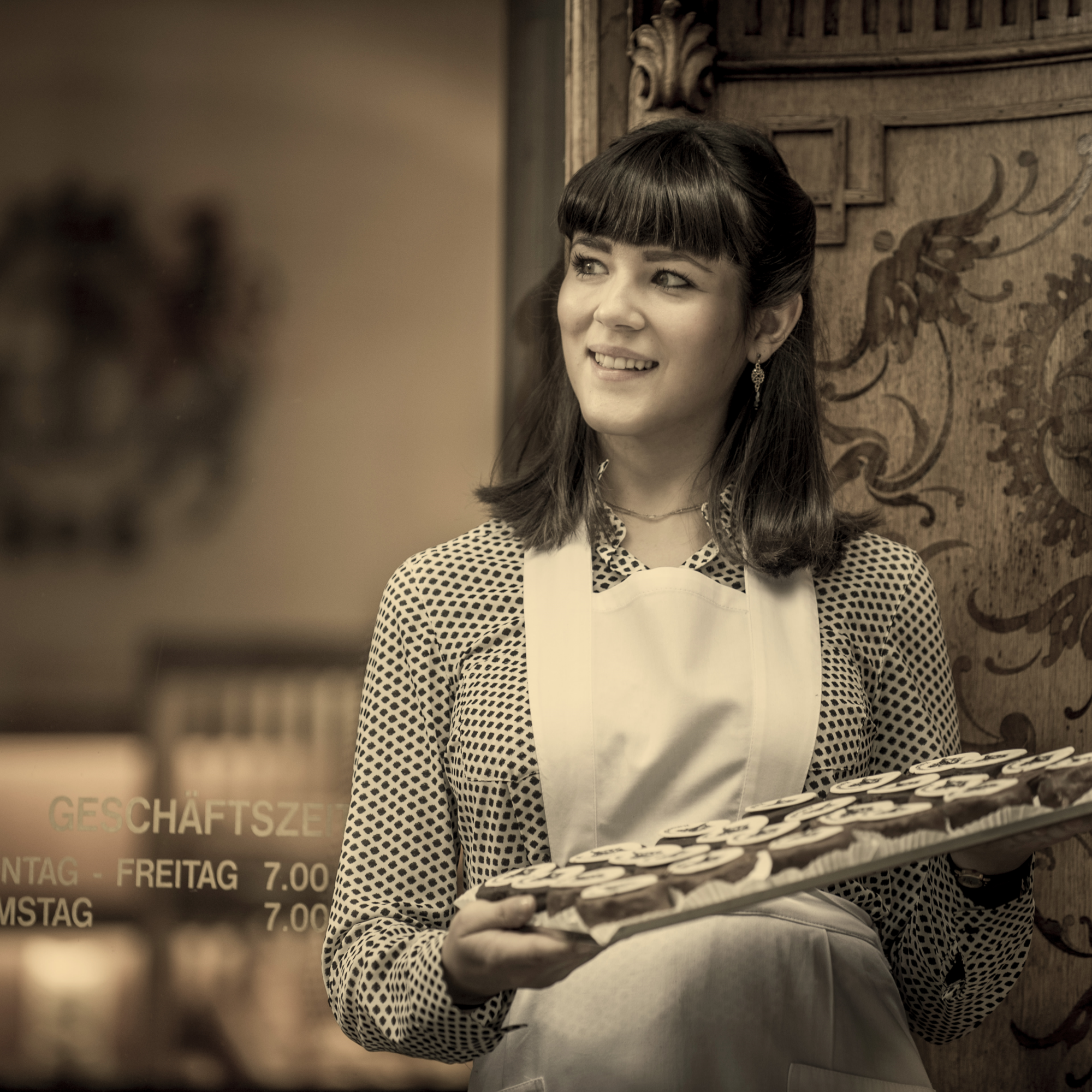 Junge Frau in Graz hält Tablett mit Süßigkeiten vor einer Tür.