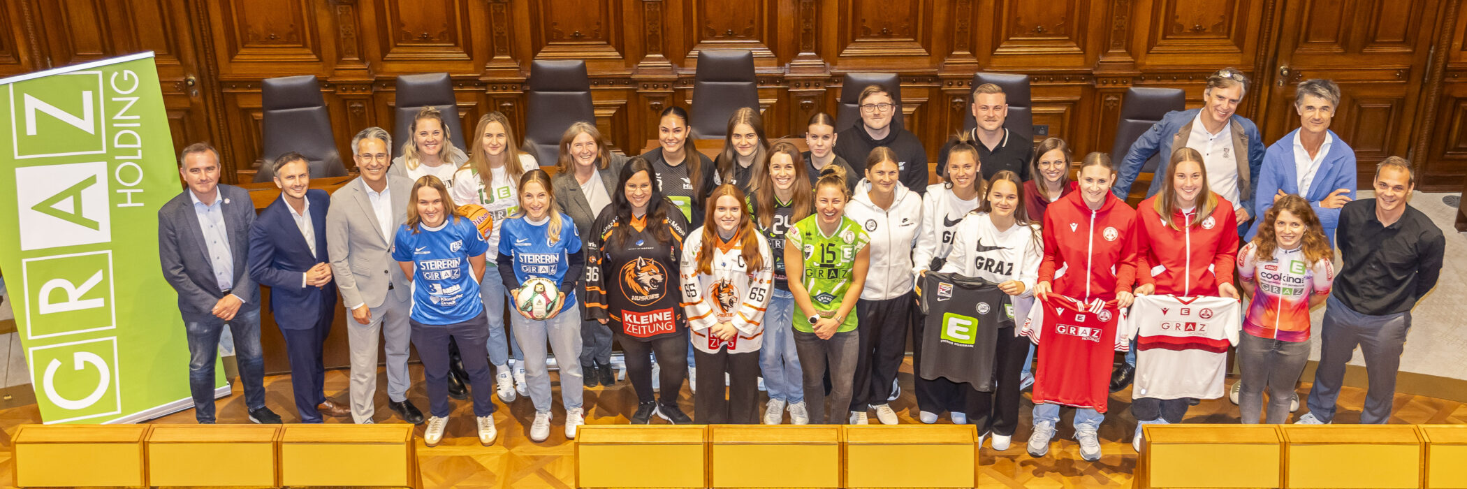 Gruppe von Sportlerinnen mit Offiziellen in Graz, Trikots mit „Graz“ und Sponsorenlogos.