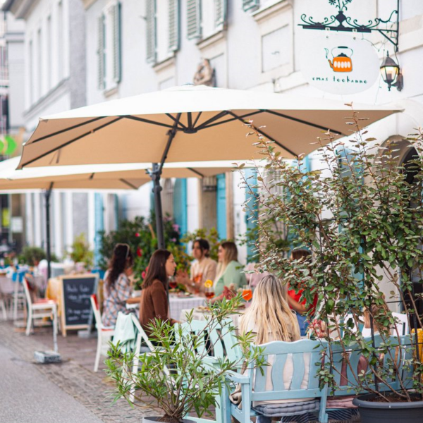 Außenbereich des „Emas Teehanne“ in Graz mit Gästen unter Sonnenschirmen.