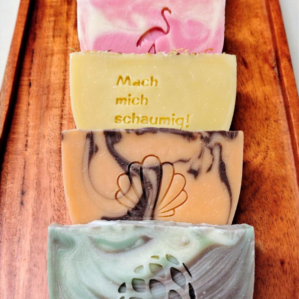 Sechs bunte Seifenstücke auf einem Holztablett. "Mach mich schaumig!" steht auf einer.