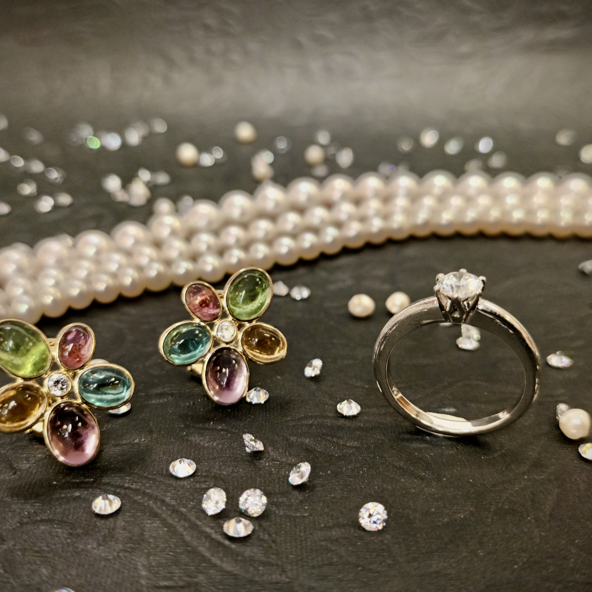 Blumenohrringe, Ring und Perlen auf schwarzem Hintergrund.