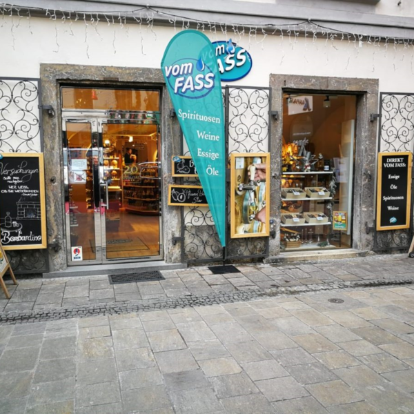 Fassade des „vom Fass“-Geschäfts in Graz mit Schildern und Auslagen.