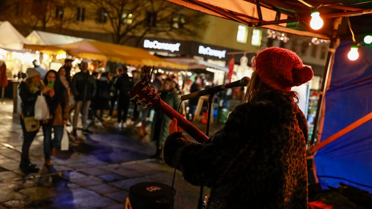 Eine Frau spielt Gitarre auf einem Markt in Graz.