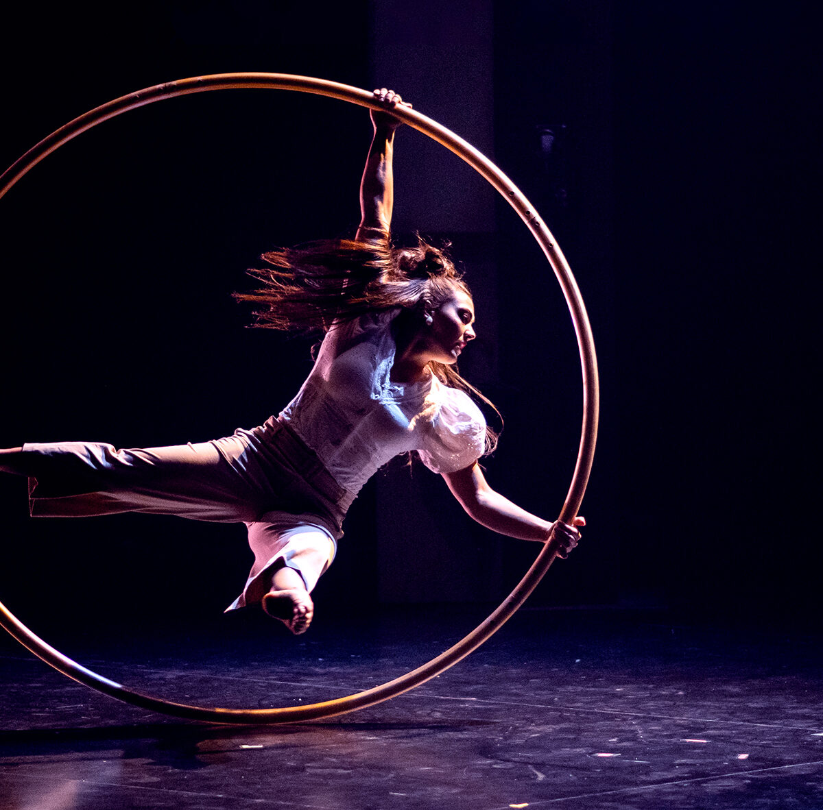 Eine Frau turnt mit einem Reifen in Graz, dunkler Hintergrund.
