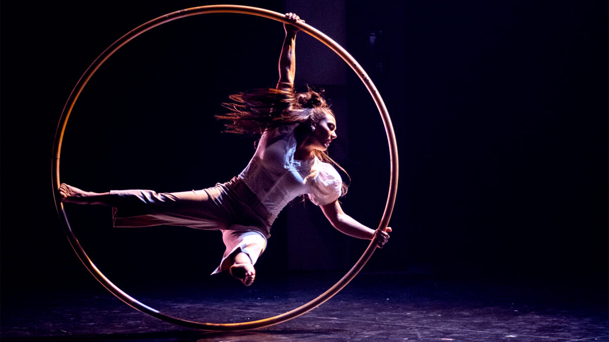 Eine Frau turnt mit einem Reifen in Graz, dunkler Hintergrund.
