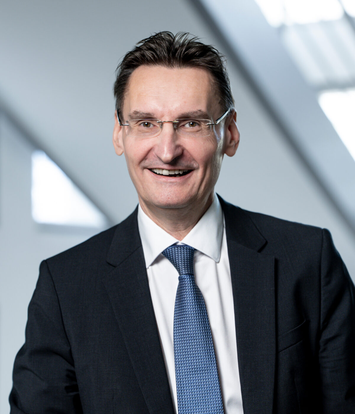 Ein Mann mit Brille, Anzug und Krawatte lächelt.