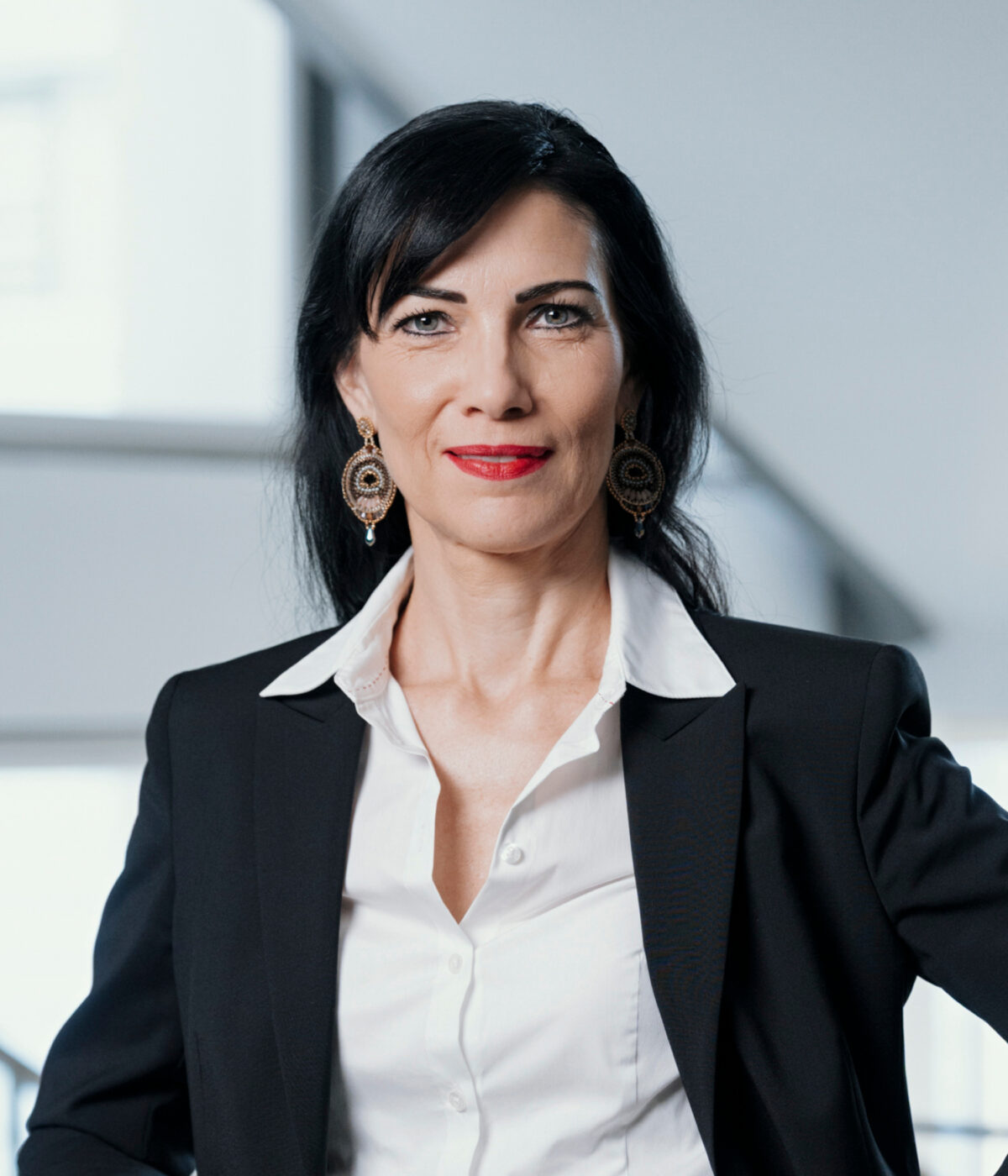 Porträt einer Frau mit dunklem Haar, Blazer und Ohrringen.