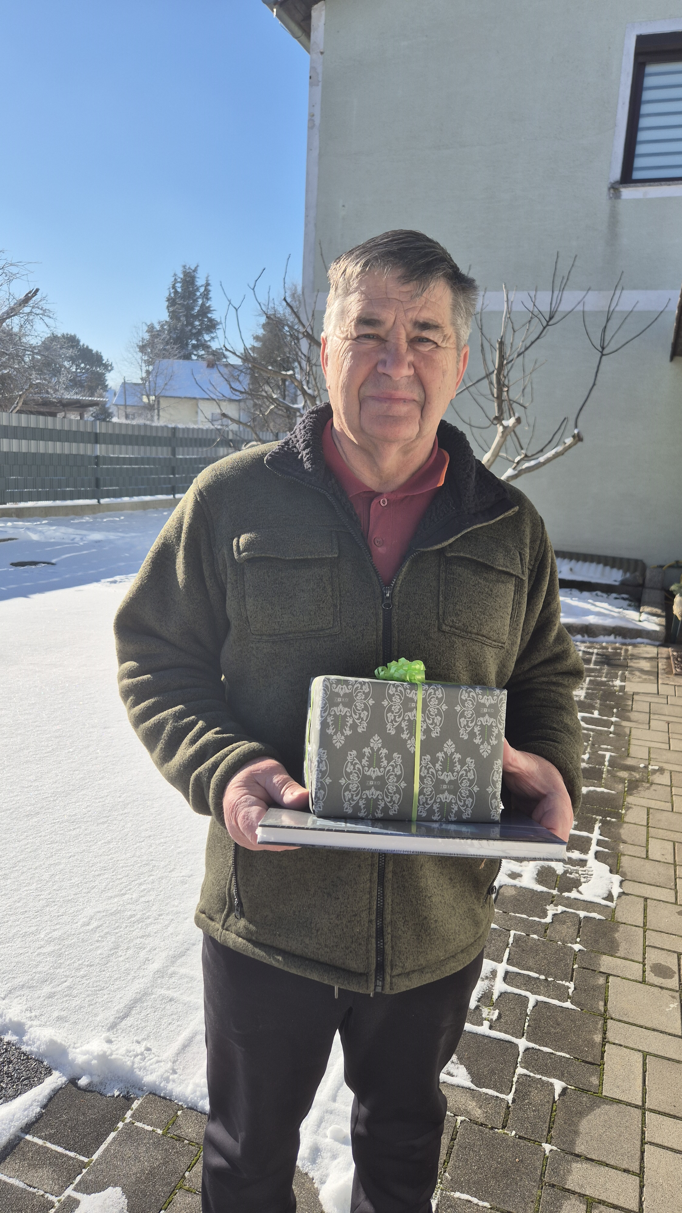 Älterer Mann hält Geschenk mit Schleife und Buch im Freien.