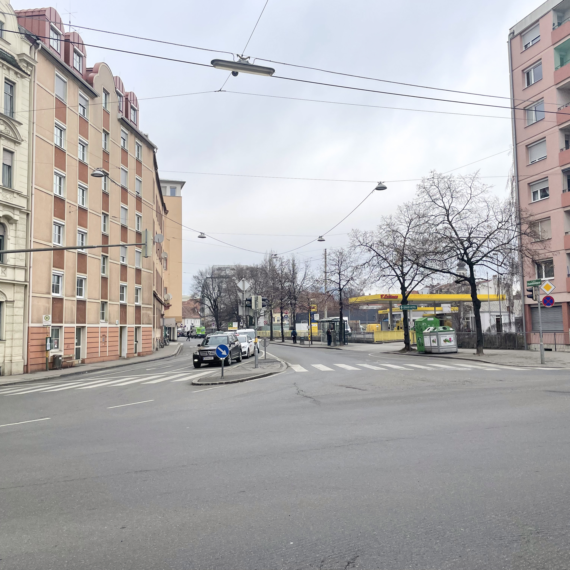 Eine Straßenkreuzung in Graz mit Gebäuden und einer Tankstelle im Hintergrund.