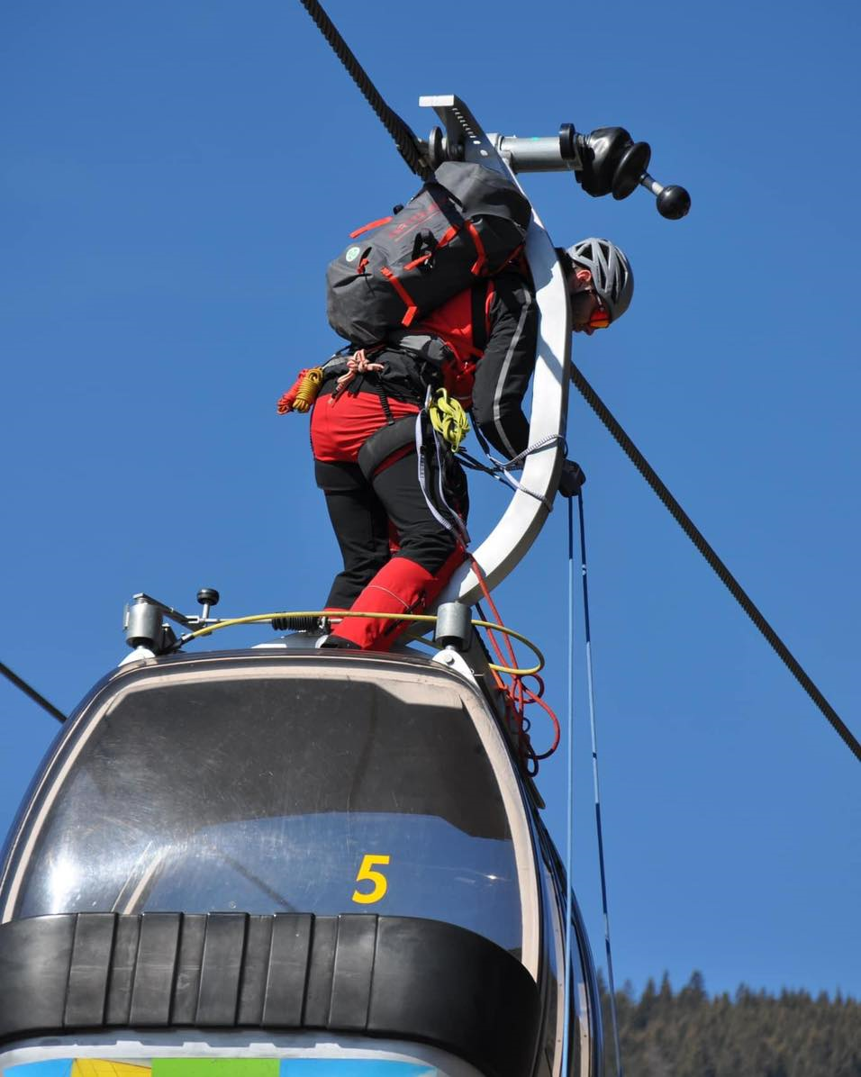 Bergretter auf Gondel Nr. 5, mit Seil und Rucksack. Blauer Himmel.