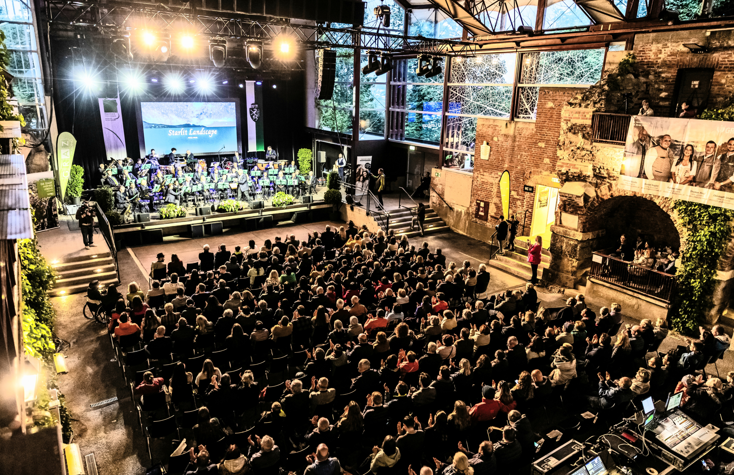 Volle Bühne in Graz, Orchester spielt, Publikum sitzt. "Starla Landscape" auf der Leinwand.