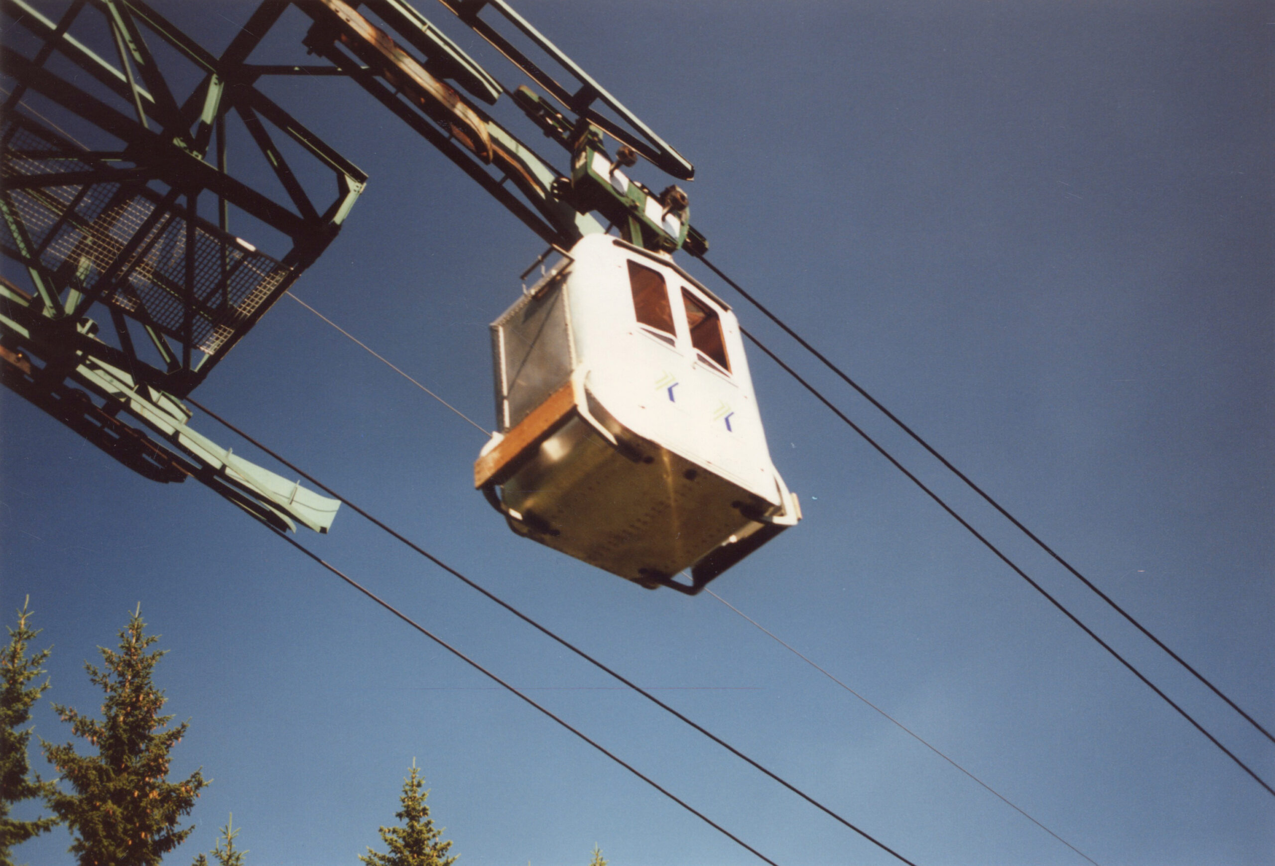 Blick von unten auf Gondel der Seilbahn Graz mit blauem Himmel.