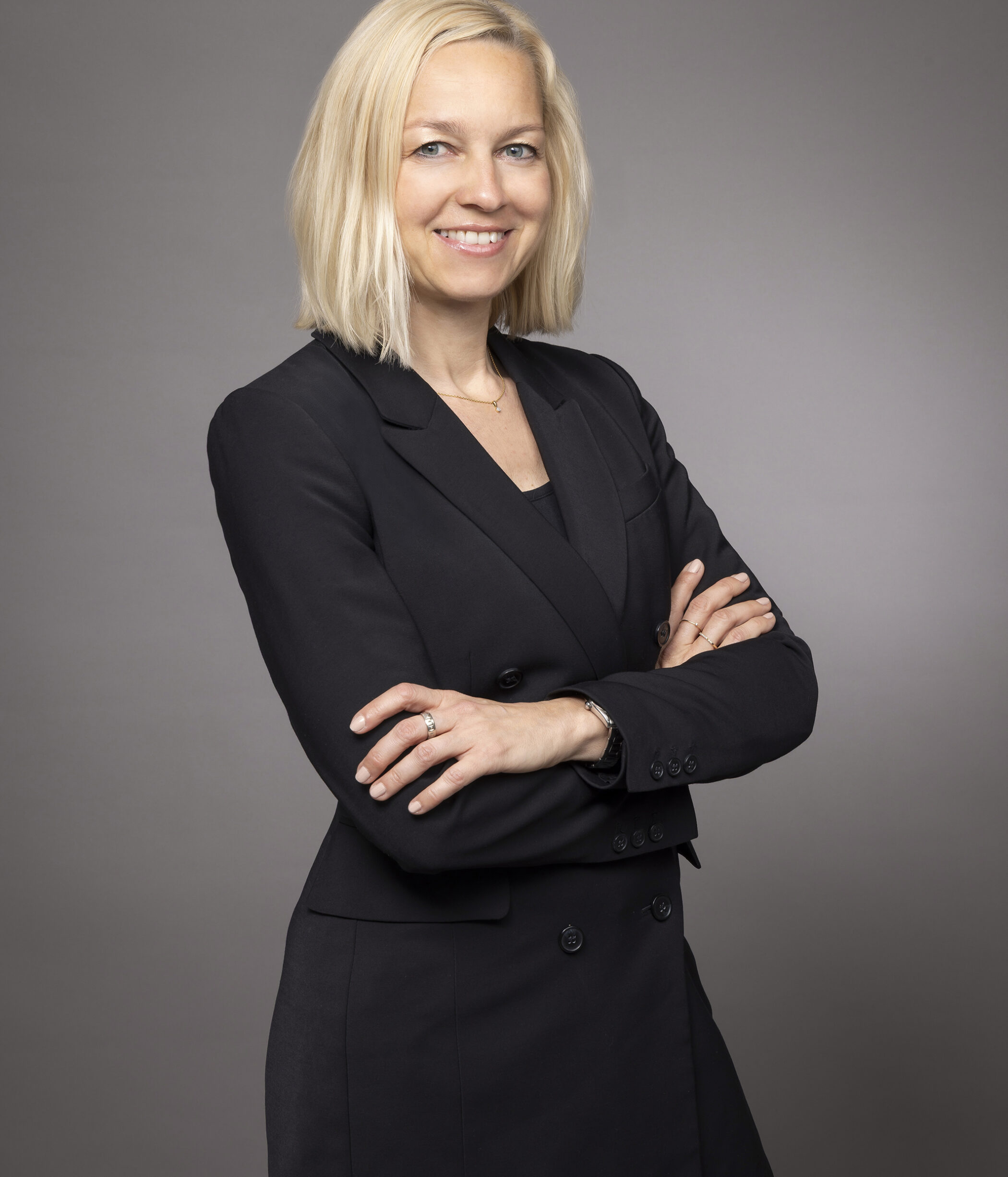 A smiling woman in a dark blazer with arms crossed.