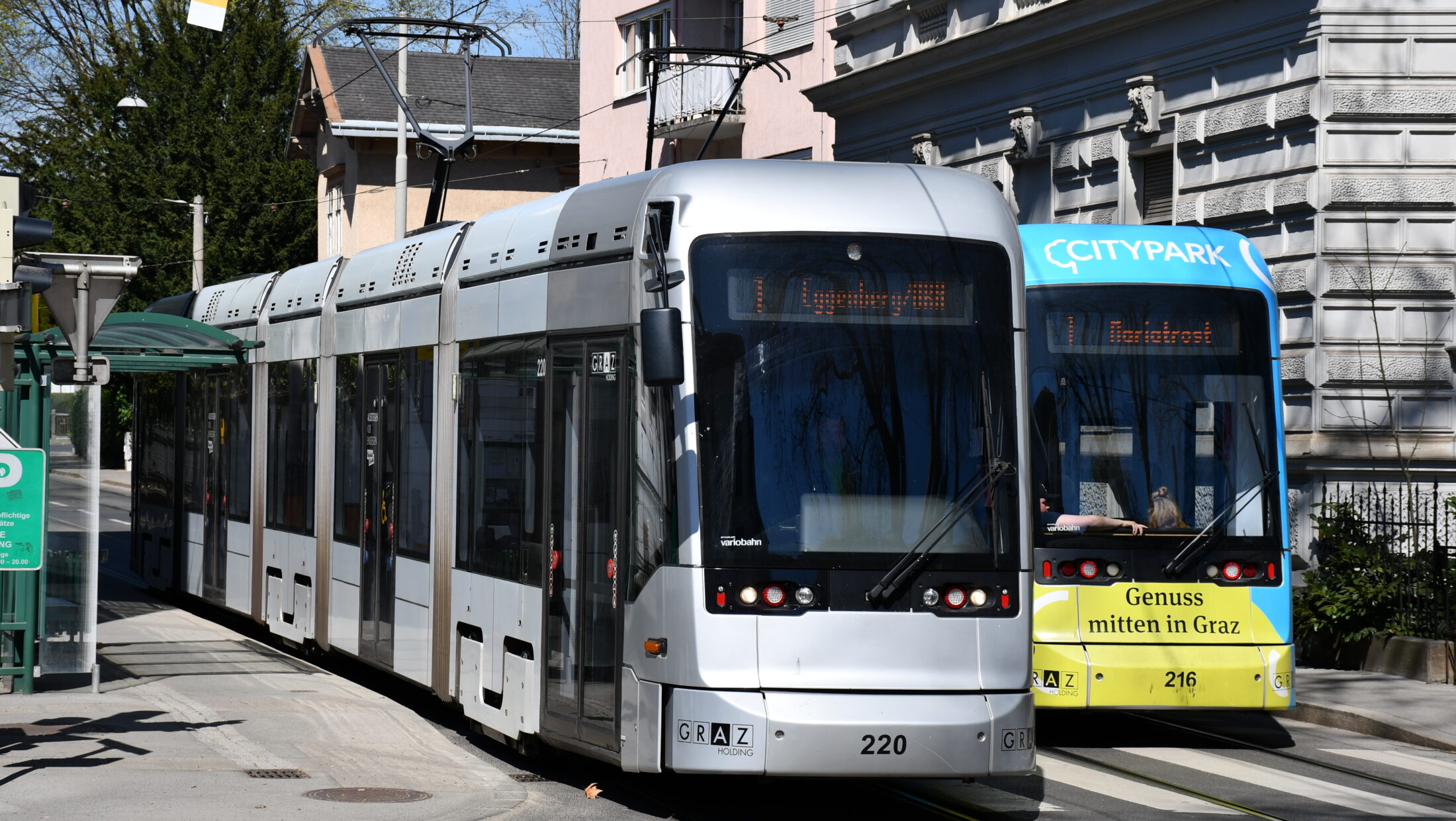 Eine silberne Straßenbahn "Graz 220" und eine gelb-blaue "Citypark" Straßenbahn.