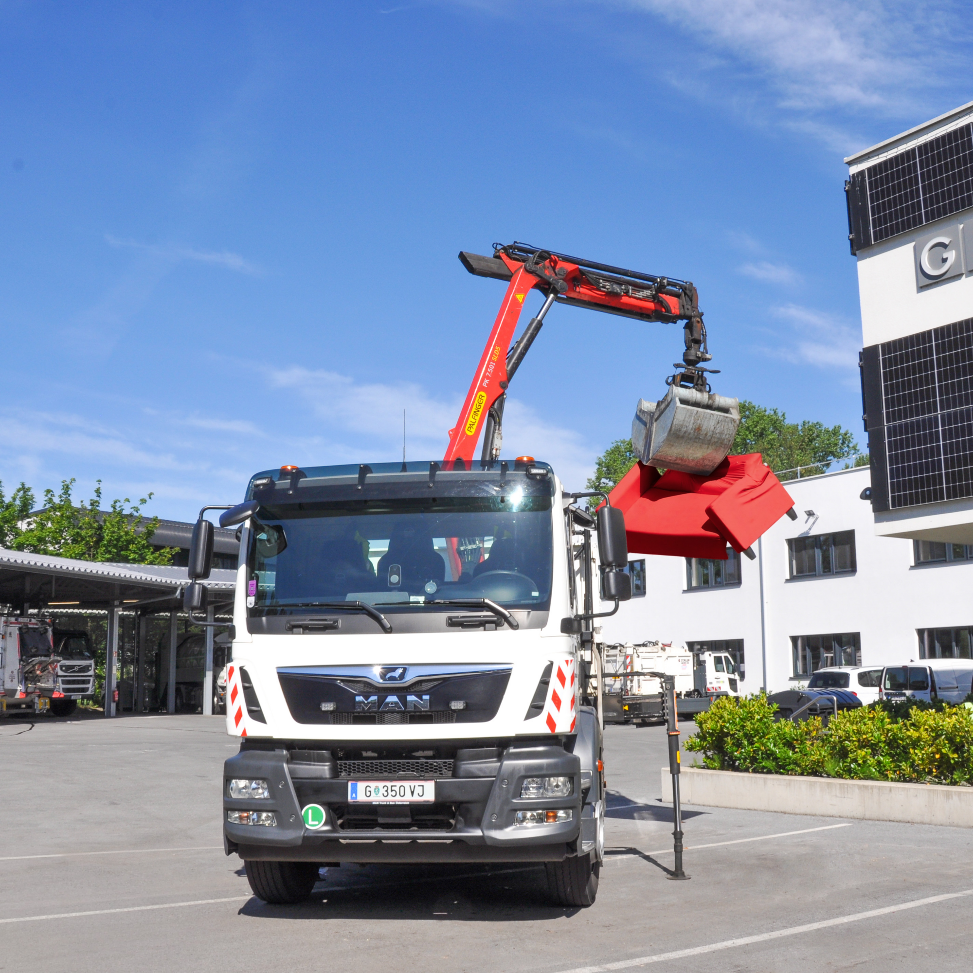 Ein LKW mit Kranarm hebt eine rote Couch auf die Ladefläche